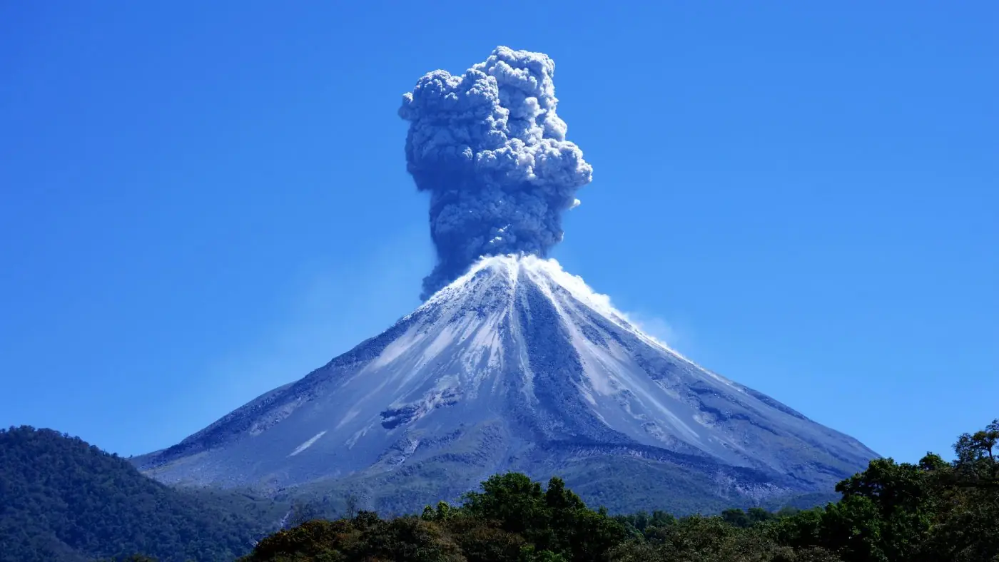 The Volcán de Colima erupting under a clear blue sky