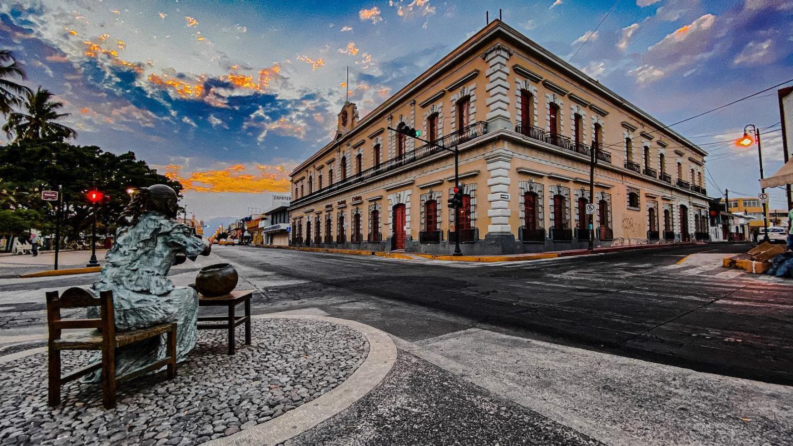 Downtown Colima at dusk — historic corner building with a bronze statue