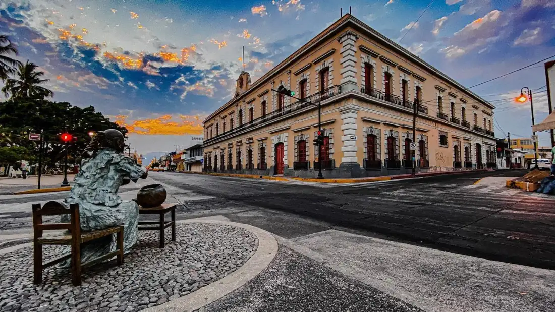 Downtown Colima at dusk: a historic corner building with a bronze statue